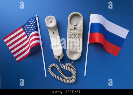 Old telephone and two flags on a blue background, a concept on the theme of telephone conversations between the USA and Russia Stock Photo