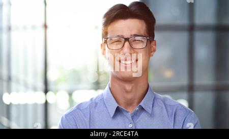 Well dressed young Asian businessman smiling confidently while standing alone in a bright modern office Stock Photo