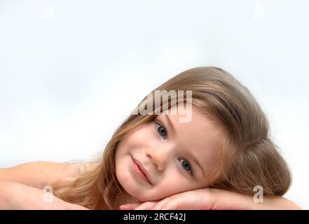 Beautiful little girl, with long hair, leans on her arms and daydreams. Stock Photo