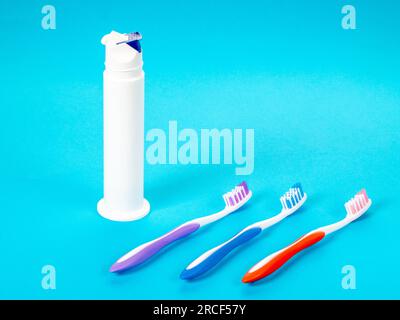 Three multi-colored toothbrushes and a tube of toothpaste on a blue background. Stock Photo