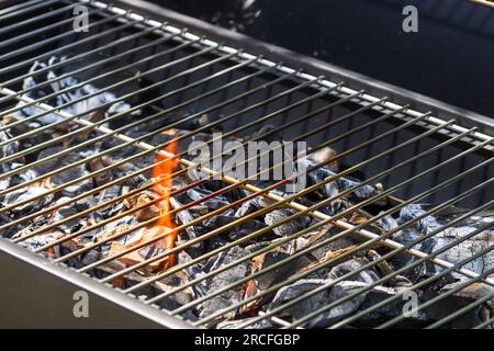 Barbecue grill pit with glowing and flaming hot open fire with red flame, hot charcoal briquettes and embers Stock Photo