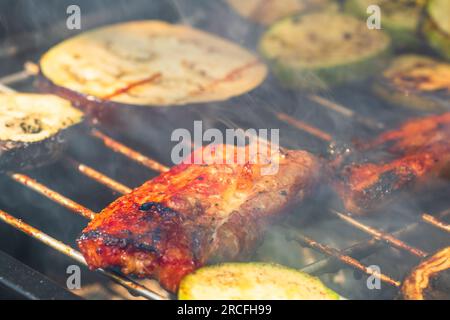 Grilling meat rolls called mici or mititei with vegetables on char barbecue. Charcoal grill with burning fire Stock Photo