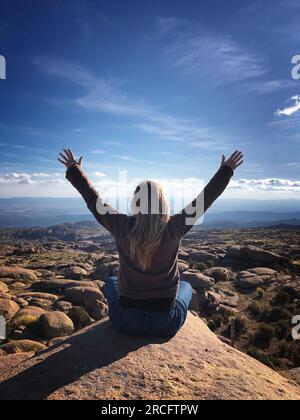 Middle-aged woman sitting on a rock contemplating the mountainous landscape and the blue sky Stock Photo