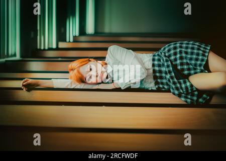 A beautiful, ginger Asian schoolgirl lies on her desk in her school uniform, exuding a mix of confidence and tranquility. Youth, identity, and the pur Stock Photo