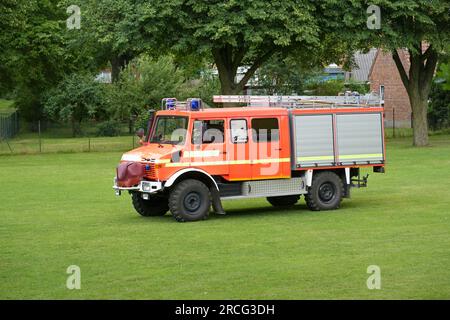 German fire engine, red orange truck with ladders on the roof and equipment for firefighting operations behind roller shutter doors on a meadow, copy Stock Photo