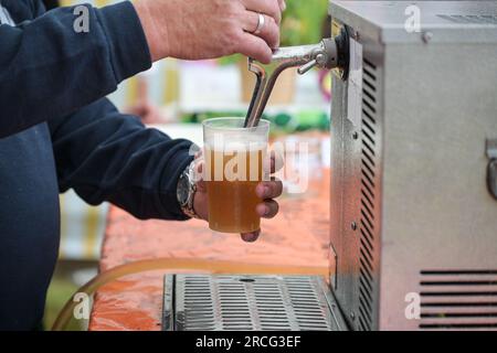Cold draught beer is poured from a mobile tap in a plastic glass at an open air summer festival, copy space, selected focus, narrow depth of field Stock Photo