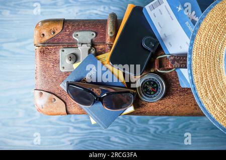 Travel accessories like passport, boarding ticket, sunglasses, mobile phone and compass on a vintage suitcase, blue wavy wooden background, top view f Stock Photo