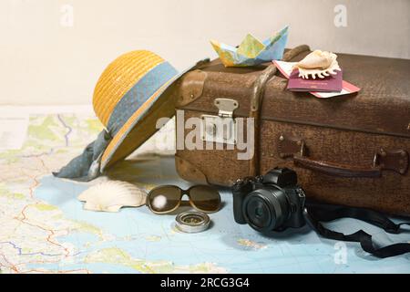 Summer vacation with a vintage suitcase, straw hat, camera, sunglasses, passport and a small paper boat on a map, travel concept, copy space, selected Stock Photo