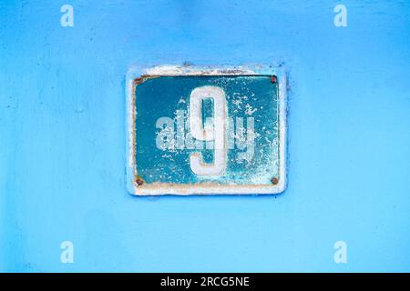 Number 9, digit nine, dark blue plate on light blue background. Stock Photo
