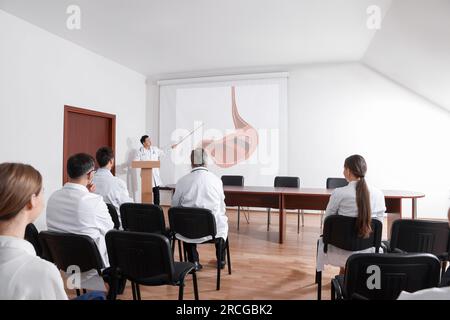 Lecture in gastroenterology. Professors and doctors in conference room. Projection screen with illustration of stomach Stock Photo