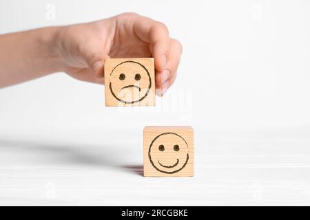 Complaint. Woman choosing wooden cube with drawn sad face instead of another one with happy on white background, closeup Stock Photo