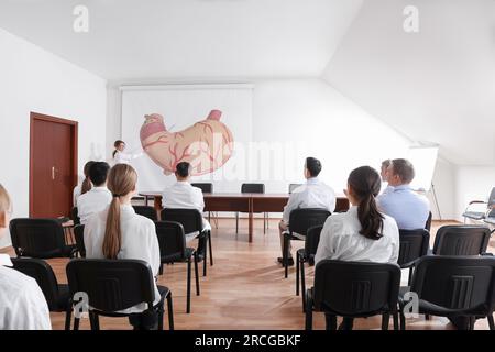 Lecture in gastroenterology. Professors and doctors in conference room. Projection screen with illustration of stomach Stock Photo