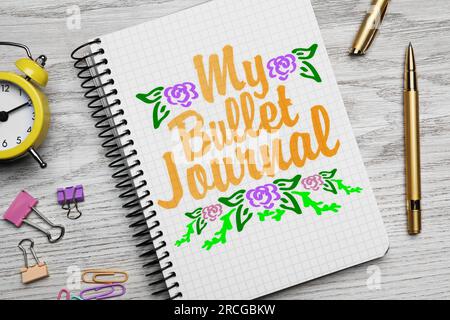 Improve your productivity. Notebook with words My bullet journal, drawn flowers, stationery and alarm clock on white wooden table, flat lay Stock Photo