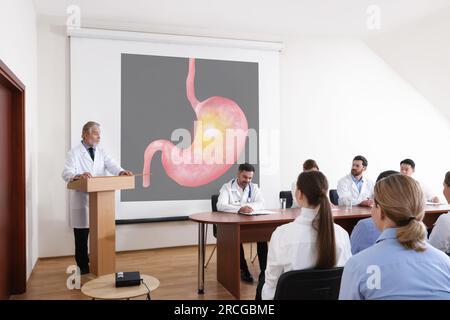 Lecture in gastroenterology. Conference room full of professors and doctors. Projection screen with illustration of stomach Stock Photo