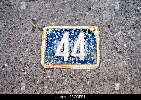 Number 44, forty-four, very old blue plate on a gray stone background. Stock Photo