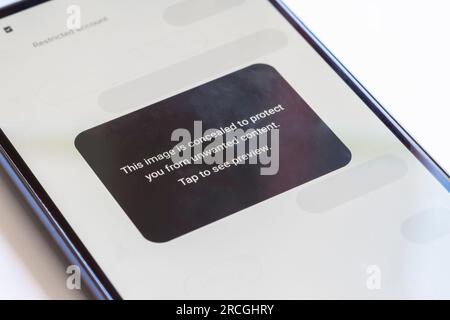 "This image is concealed to protect you from unwanted content" warning the user of harmful content on social media displaying on a mobile phone, UK Stock Photo
