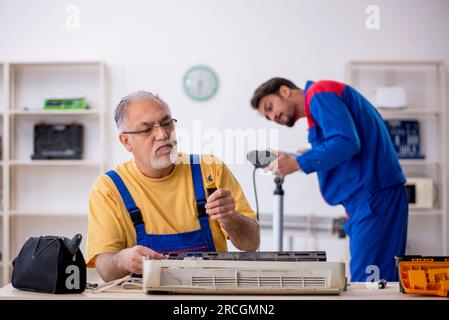 Two repairmen repairing air-conditioner at workshop Stock Photo