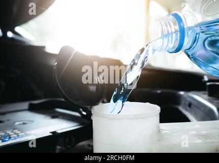 Close up of a bottle of water being poured into a windshield washer tank. Stock Photo
