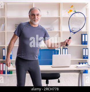 The white bearded old man employee doing exercises in the office Stock Photo