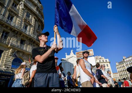 Marseille, France. 14th July, 2023. A parade spectator waves a large French flag, celebrating the French 14th of July. Approximately 900 military personnel and equipment from all three branches of the French armed forces, as well as national security and emergency services, participated in a grand parade through Marseille's Old Port to commemorate Bastille Day on the 14th of July. Credit: SOPA Images Limited/Alamy Live News Stock Photo