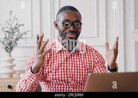 Ecstatic black man in glasses, reading laptop news, celebrates office success; a joyful African employee. Stock Photo