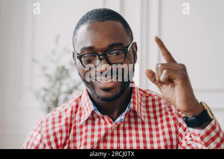 Cheerful African English tutor, glasses, explaining homework online; businessman happily conversing with colleagues on video call. Stock Photo