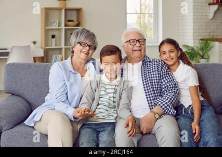 Portrait of grandparents sitting with their grandchildren on sofa at home and looking at camera. Stock Photo