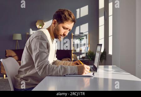Young business man working with laptop computer at home or at office and writing. Stock Photo
