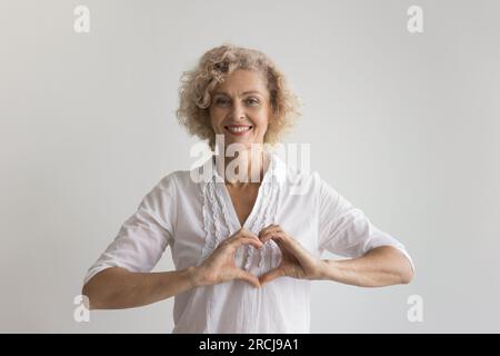 Happy pretty mature lady making heart shaped fingers Stock Photo