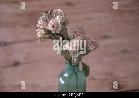 Blue glass vase with small bouquet of dried roses on wooden table Stock Photo