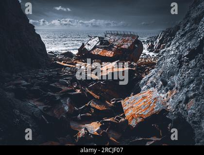 Rusted ship by rocky cliffs on beach Stock Photo