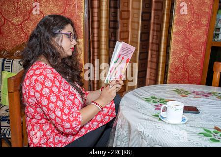 A smart girl is sitting on a chair at a table, reading a book in a cozy and comfortable home environment Stock Photo
