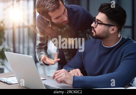 two male colleagues are talking at the table in the office. Stock Photo