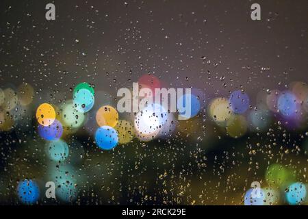 Blurred lights of city night view from behind glass with raindrops Stock Photo