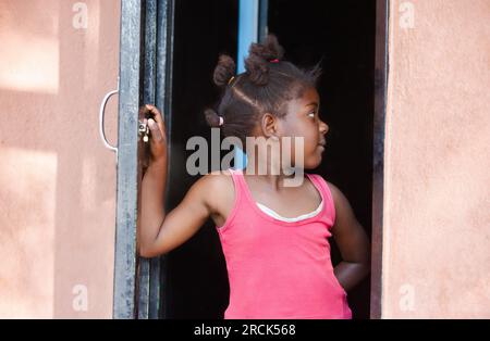 profile portrait happy small african girl with ponytails standing in the door frame at her home in the township Stock Photo