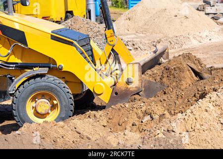 The powerful pneumatic sliding bucket of the wheeled bulldozer works on the leveling of the earthen working platform. Stock Photo