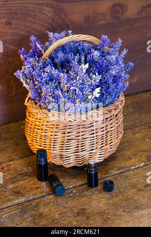 Fresh lavender (Lavandula angustifolia) in a wicker basket and essential oil bottles on a wooden table Stock Photo