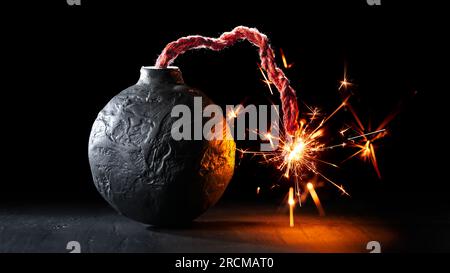 Round black bomb with lit fuse burning with sparks. Bomb about to detonate symbolizing destruction, threats, or dangerous violence. Stock Photo