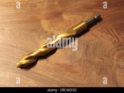 A Large Gold Metal Drill Bit on a Wooden Background Stock Photo