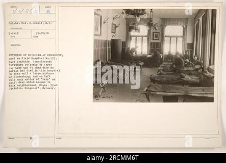 Interior of building at Rengsdorf, Germany, used as Field Hospital No.127 during World War One. The photograph, taken on December 25, 1918, shows the ward containing convalescent Influenza patients of the three-day type. Notably, no deaths had occurred in this hospital up to that date. The rear wall prominently features a large picture of Hindenburg, while the left wall is adorned with several antlers from small deer, a common sight in the area. The building served as headquarters for the 32nd Division. Stock Photo