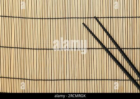 Pair of black chopsticks on bamboo mat, top view. Space for text Stock Photo