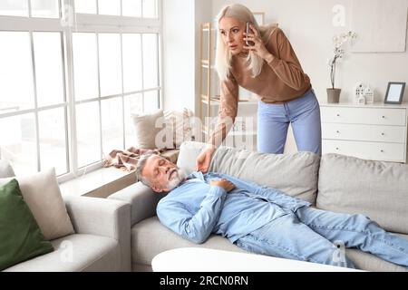 Mature woman calling ambulance while her husband having heart attack at home Stock Photo