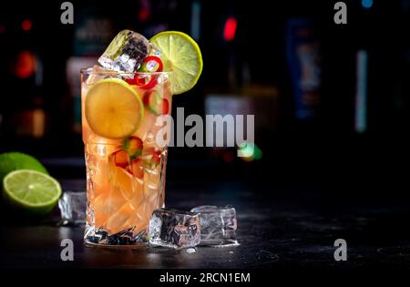 Siam sunrays alcoholic cocktail drink with vodka, coconut liqueur, ginger, chili pepper, soda, lime juice, dark background, bar tools and bottles Stock Photo