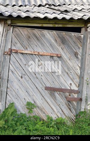 Old aged weathered wooden barn shack door, grey wood boarding hut wall planks, rusted metal hinges, rusty paint zinced texture grunge vertical closeup Stock Photo