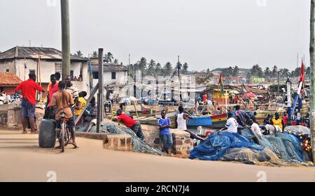 A photo of buildings and group of young men watching the fishing boats and the men working aboard them in Cape Coast, Ghana, West Africa. Stock Photo