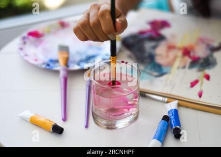 Woman dipping paintbrush into water on a table with and paints and palette Stock Photo