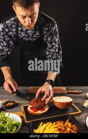 Chef puts beef patty on a burger loaf. Delicious and harmful food, fast food Stock Photo
