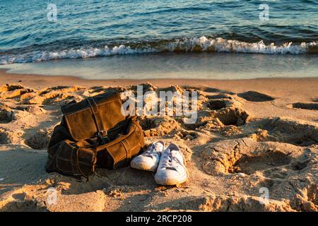 Travel and vacation concept. White sneakers and stylish brown backpack on a sandy beach. Baltic Sea, Hel, Pomerania, Poland Stock Photo
