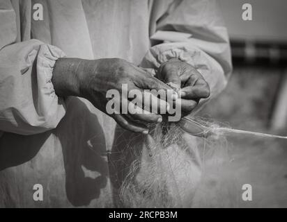 A Vietnamese fisherman wearing an orange raincoat repairs his fishing nets on My Khe beach in Son Tra, Danang, Vietnam. Stock Photo