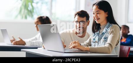 Happy young girl getting assistance from her teacher as she engages in a computer science lesson. Female student learning and understanding the basics Stock Photo